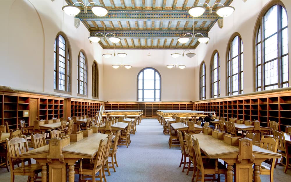 Wilson Library interior showcasing wooden bookshelves and natural light from large arched windows.