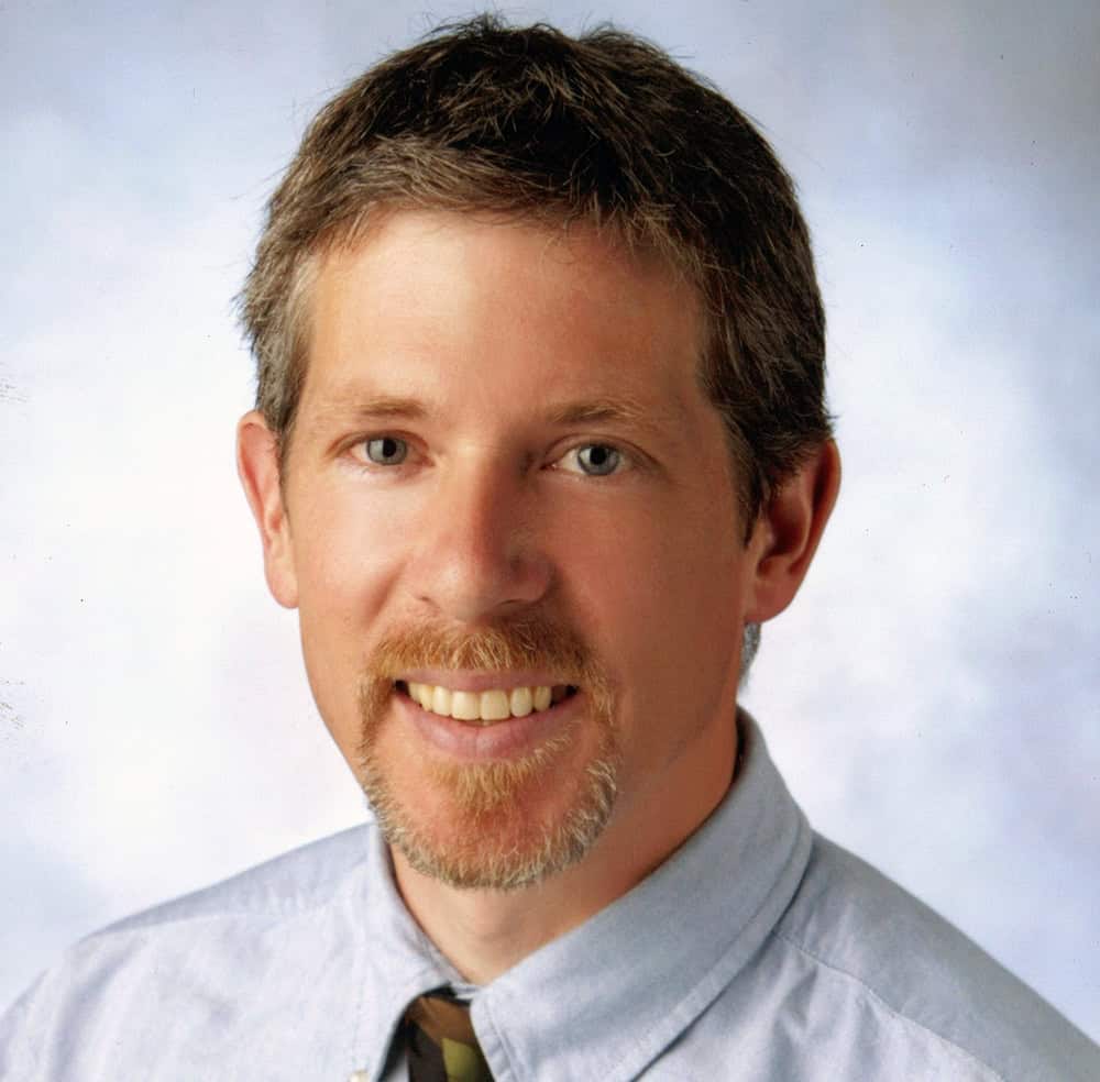 Portrait of a smiling man with light brown hair and a beard, wearing a light blue shirt.